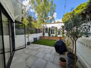 A patio with a table and chairs, a small lawn, and a white building with arched windows. - Chic Property With Backyard Near Emirates Stadium (Greater London)