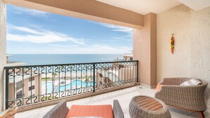 A balcony with a view of a pool and beach, wicker furniture, and a railing. - Beautiful Beachfront Retreat With Panoramic Ocean Views (Backus)