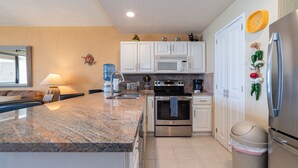 A modern kitchen with granite countertops, stainless steel appliances, and white cabinetry. - Beautiful Beachfront Retreat With Panoramic Ocean Views (Backus)