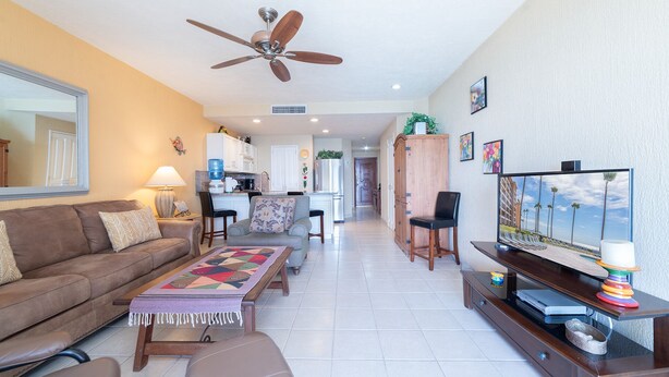 A living room with a sofa, coffee table, TV, and a ceiling fan. - Beautiful Beachfront Retreat With Panoramic Ocean Views (Backus)