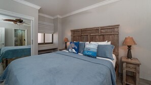 Ein Schlafzimmer mit einem Bett, zwei Nachttischen, einem Deckenventilator, einem Fenster mit Jalousien und einem hölzernen Kopfteil.