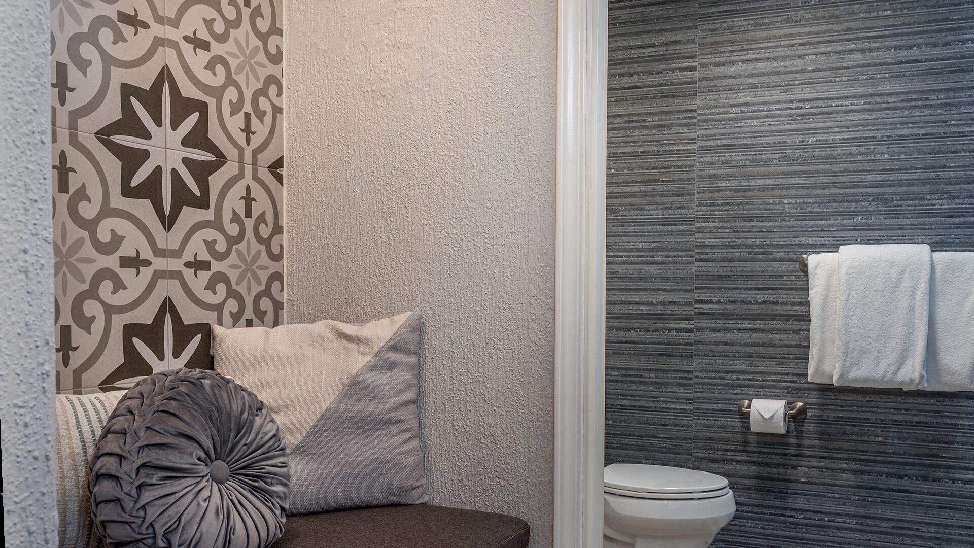 A bathroom with a patterned wall, a toilet, and a towel rack with towels.