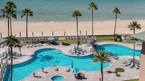 A resort pool with lounge chairs and palm trees, overlooking a beach. - Stunning Oceanfront Escape With Sweeping Sea Views (Puerto Peñasco)