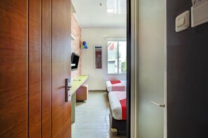 Un pasillo que conduce a una habitación con una cama, un escritorio y un televisor.