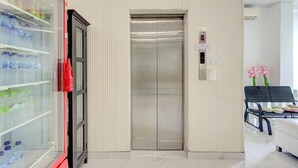 A hotel lobby with a vending machine, an elevator, and a seating area with a bench and a chair. - Stylish Twin Suite Escape W/ Free Wifi and Parking (Jakarta)
