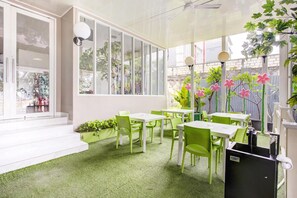 Un espacio interior luminoso con sillas y mesas verdes, ventanas amplias y un ventilador de techo.