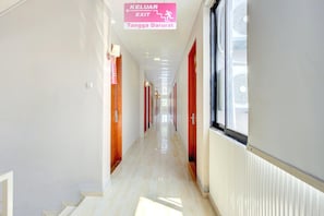 A hallway with a sign indicating an exit, a radiator, and a window. - Stylish Twin Suite Escape W/ Free Wifi and Parking (Jakarta)