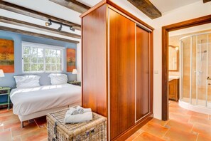 A bedroom with a bed, a wooden wardrobe, a wicker basket, and a shower area.
