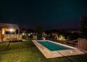 Une piscine avec une terrasse en bois, un espace abrité et une vue sur la ville la nuit.
