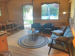 Une piĂšce comprenant un canapĂ©, des fauteuils, une petite table, un tapis et une fenĂȘtre donnant sur une piscine et des arbres.