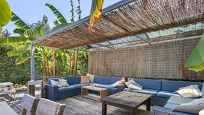 An outdoor seating area with a thatched roof, wooden furniture, and a backdrop of banana plants. - Boavista Glamping Tent with Mountain View, Private Pool and Wi-Fi (Arco de Baúlhe)