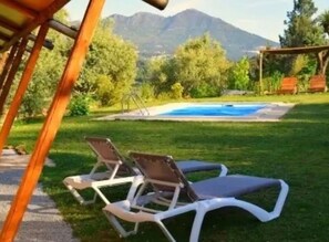Un espace aménagé au bord de la piscine, avec des chaises longues, une pergola et une vue sur la montagne.