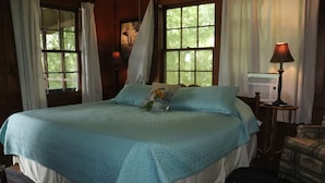 Una cama con un edredón azul, una lámpara de noche y una ventana con cortinas.