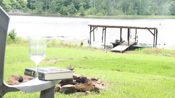 Vista del lago con muelle de madera, una copa de vino y un libro titulado 'El Testamento de C.S. Lewis' sobre una mesa.