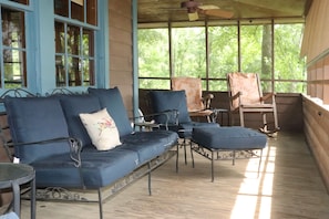 A covered porch with a blue sofa, two chairs, and a small table.