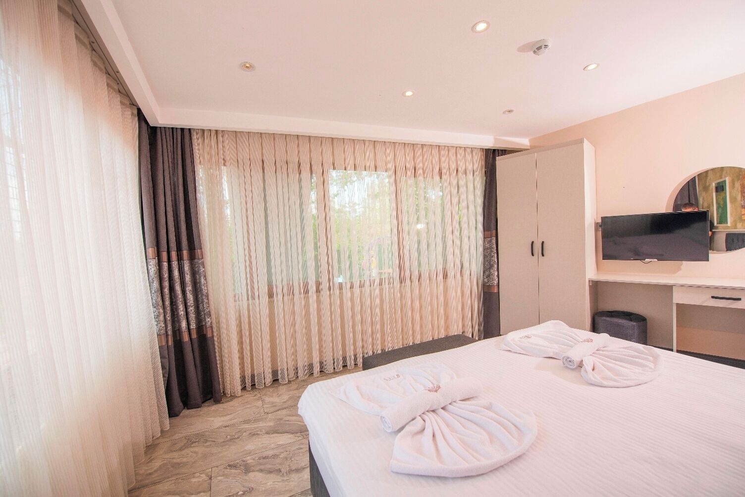 Una habitación de hotel con cama, cortinas, televisor y escritorio.