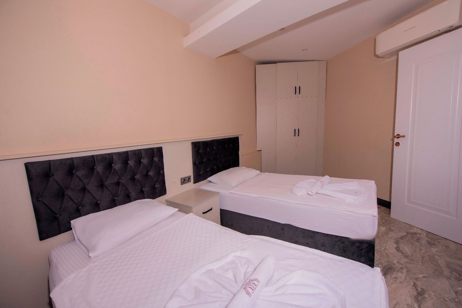 Ein Hotelzimmer mit zwei Betten, einem Schrank, einem Nachttisch und einer Tür.