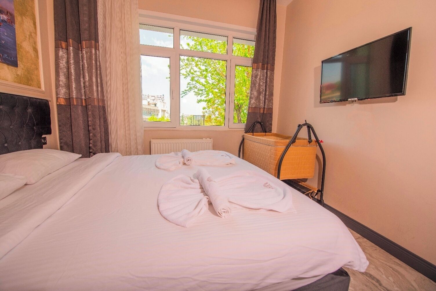 A hotel room with a bed, a television on the wall, and a window with curtains.