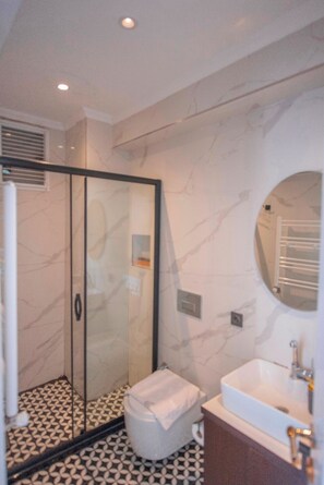 Un baño con cabina de ducha de vidrio, un lavamanos blanco y suelo con estampado de mármol.