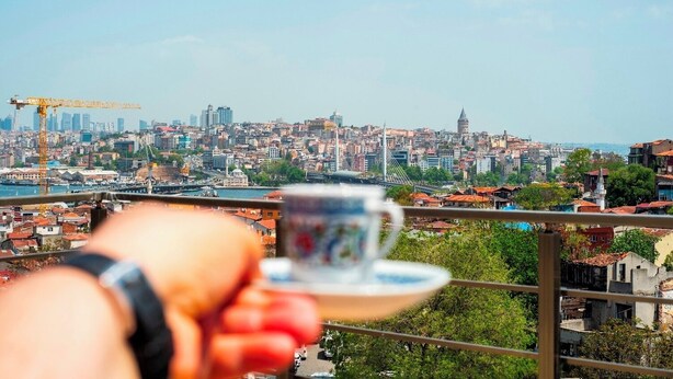 A hand holding a cup, overlooking a cityscape with buildings, a bridge, and a body of water. - Mar boutique's luxury apartment (FATIH)
