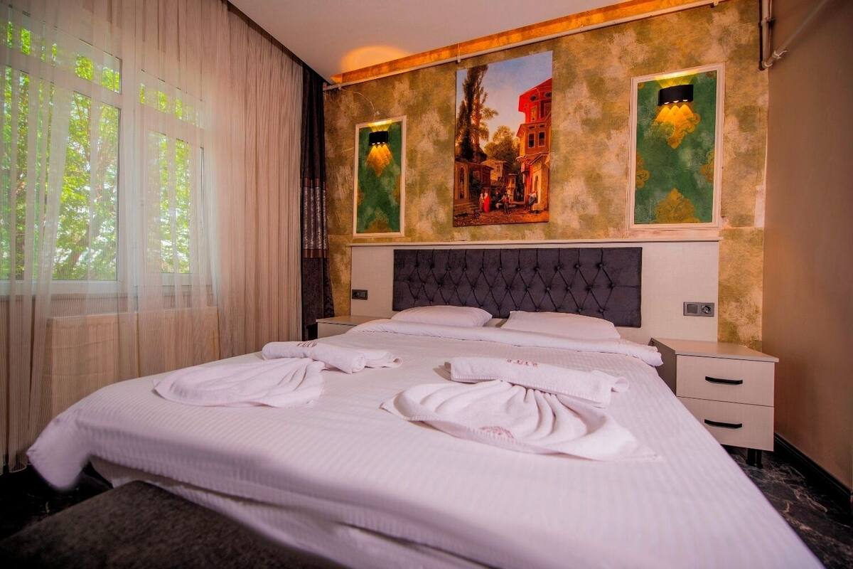 Een hotelkamer met een groot bed, twee nachtkastjes, een hoofdeinde en twee schilderijen aan de muur.