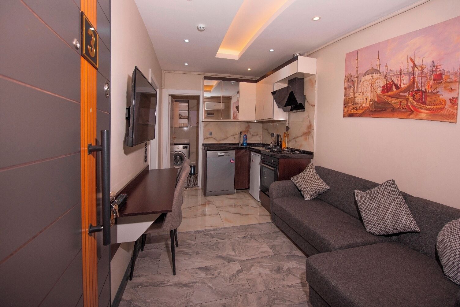 Un espace de vie compact comprenant un canapé, une table à manger, un coin cuisine et un téléviseur fixé au mur.