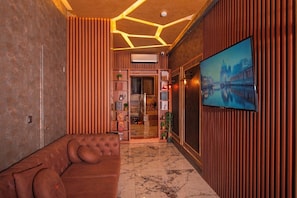 Een modern interieur met een bruine leren bank, een marmeren vloer, houten lambrisering en een groot televisiescherm waarop een stadsbeeld te zien is.