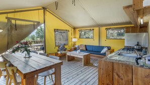 A tented accommodation with a dining area, sofa, and kitchenette.