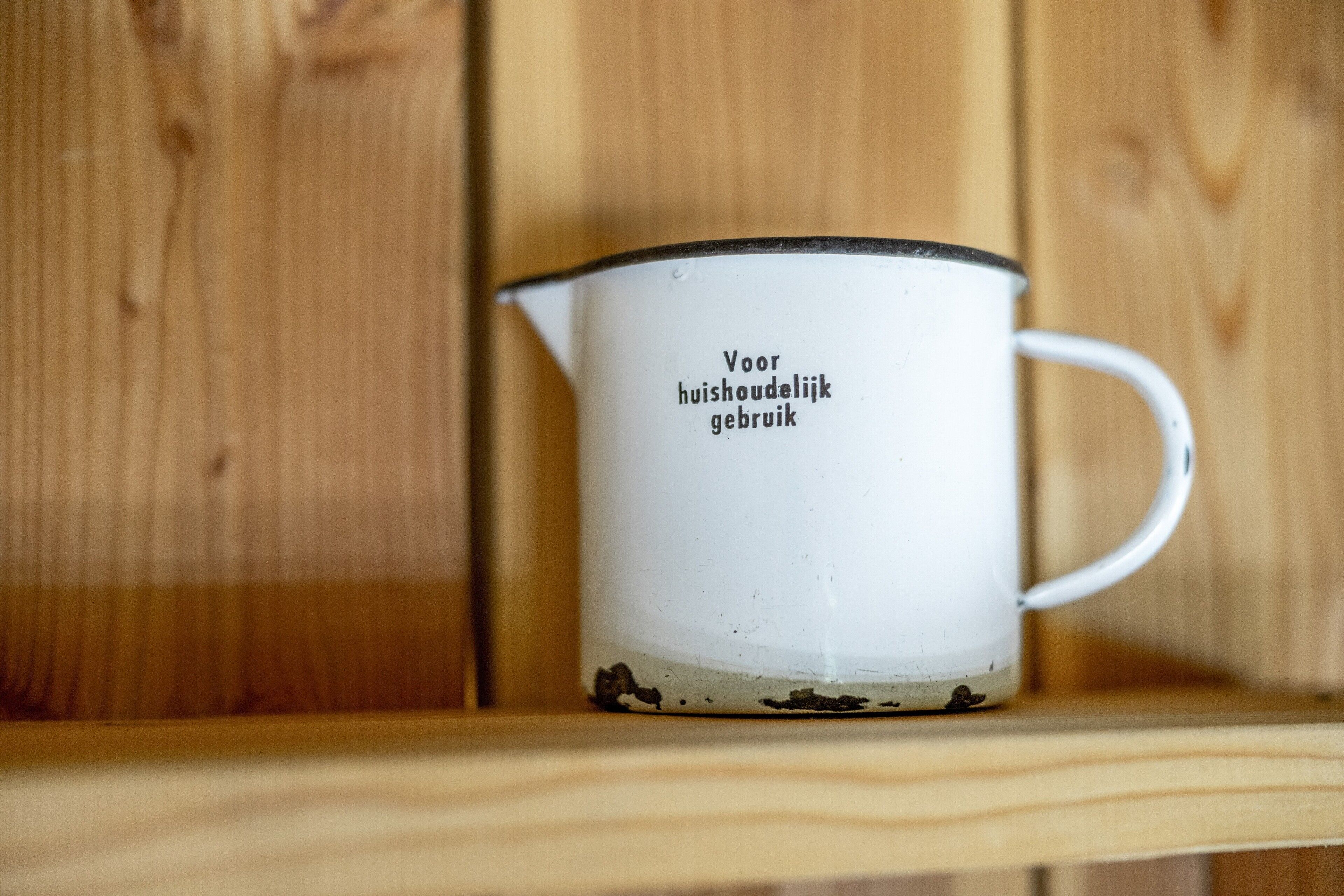 A white ceramic mug with black text on a wooden shelf.