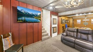 A room with a mounted TV, a sofa, a bench, a staircase, and a wall with hunting-themed decorations. - Santa Fe 1976! Work Travel Stay Awhile Game Room! (Ottawa)