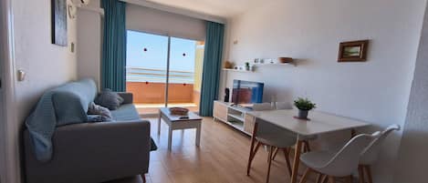 Un soggiorno moderno con divano, tavolo da pranzo con sedie, televisore e balcone con tende.