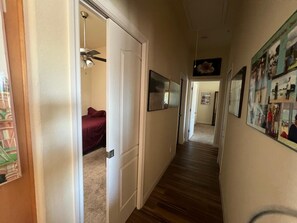 Ein Flur mit einer zurückliegenden Schlafzimmertür, einem Deckenventilator und einer Wand mit gerahmten Bildern.