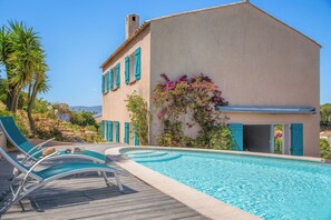 Ein Poolbereich mit Liegestühlen, einem Pool und einem Gebäude mit blauen Fensterläden und einem Garten.
