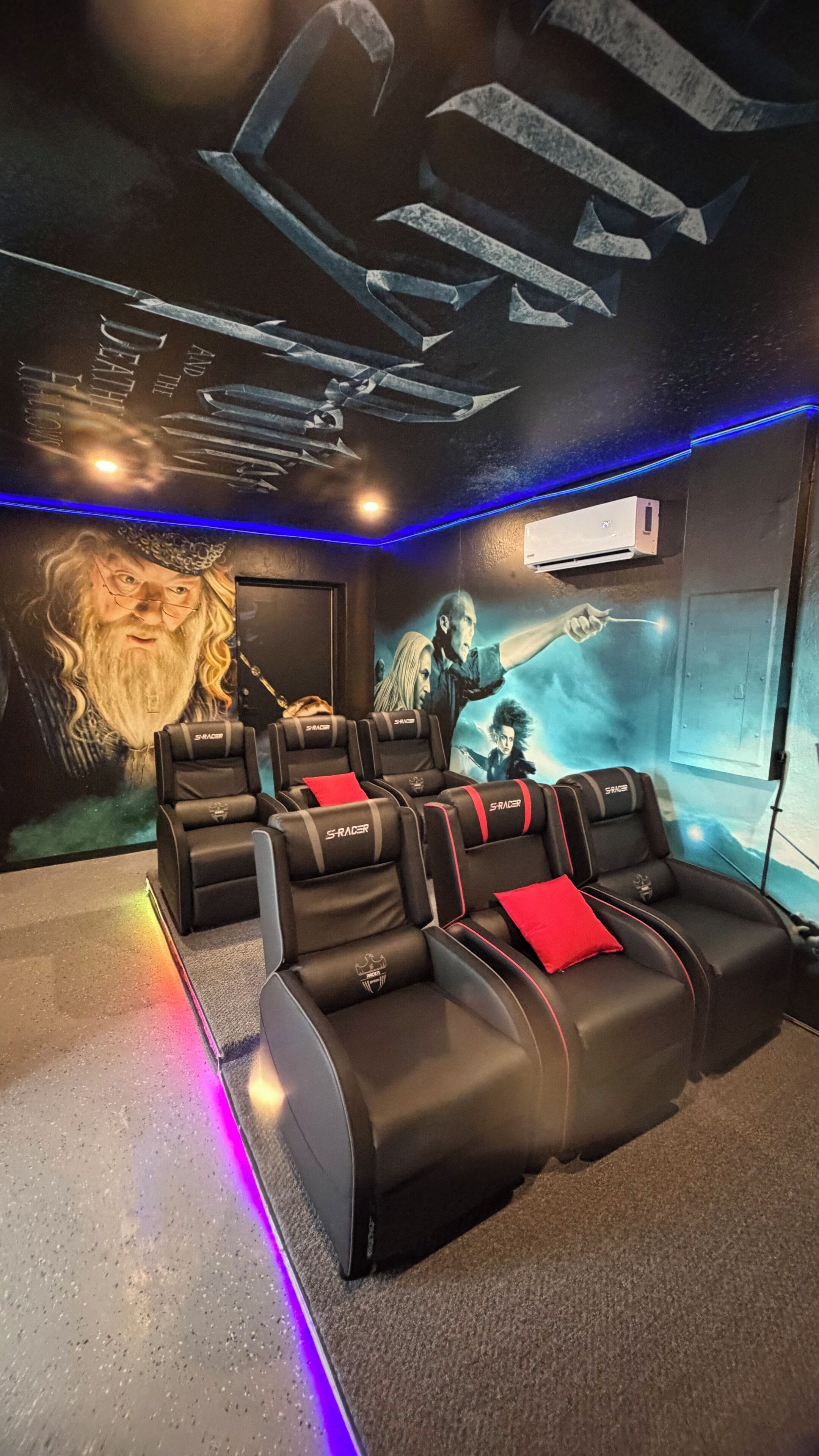 A theater with black leather seats, a large movie poster, and blue ambient lighting.