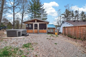 A wooden cabin with a large window, a hot tub, and a gravel driveway.