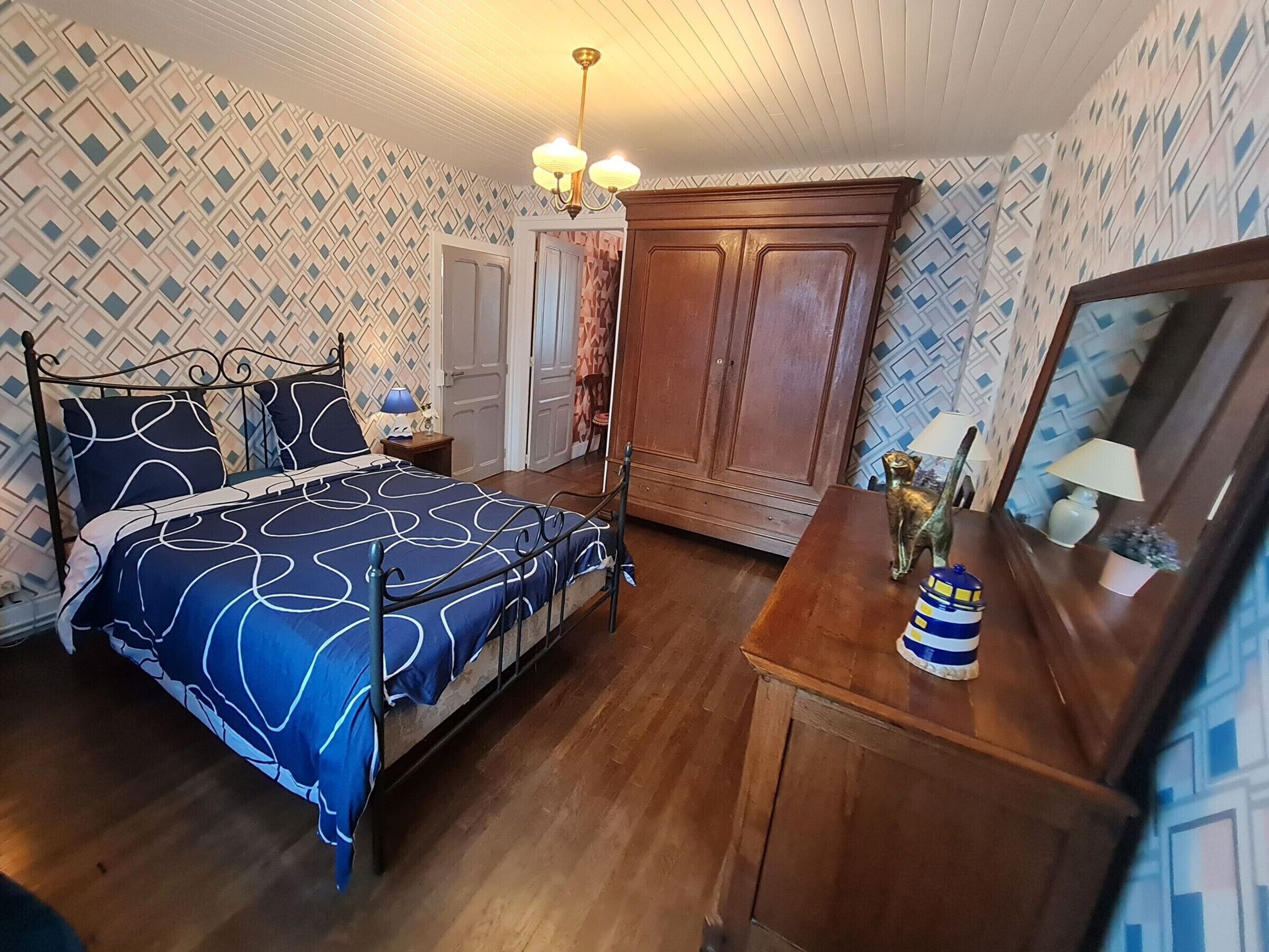 A bedroom with a bed, a wooden dresser, a mirror, and a wardrobe.