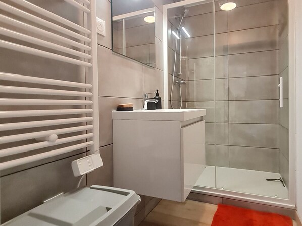 Une salle de bain moderne avec une douche Ă parois de verre, un lavabo blanc et un porte-serviettes.