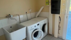 Un cuarto de lavandería con un lavamanos, dos lavadoras, una secadora y un televisor montado en la pared.