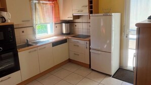 Cocina compacta con armarios blancos, horno empotrado, refrigerador y ventana con cortina.