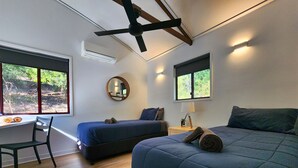 Une chambre avec deux lits, un bureau, une chaise, un ventilateur de plafond et une fenêtre donnant sur un paysage verdoyant.