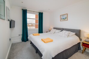 Una camera da letto con un letto, tende, una lampada da comodino, una televisione e un quadro appeso al muro.