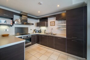 Una cucina moderna con mobili scuri, elettrodomestici in acciaio inossidabile e pavimento piastrellato.