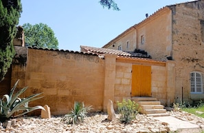 Un edificio de piedra con tejado de baldosas, puerta de madera y una pequeña escalera que lleva a la entrada.