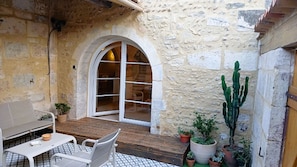 Un patio de paredes de piedra con una mesa y sillas de madera, un sofá blanco y una gran planta de cactus.