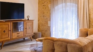A living room with exposed wooden beams, a television on a wooden cabinet, a sofa, and a large window with curtains. - Mas de l'Amarine Between Camargue and Provence (Bellegarde)