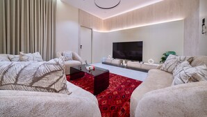 A modern living room with a flat-screen TV, two sofas, a coffee table, and a red patterned rug. - A comfortable 2 bedroom apartment in Al-Hamra (Jeddah)