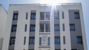 A multi-story building with a central logo, multiple windows, and a parking area in front. - A comfortable 2 bedroom apartment in Al-Hamra (Jeddah)