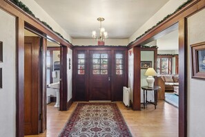 A hallway with a wooden door, a chandelier, a radiator, and a patterned rug.