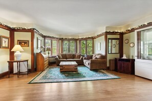 Una habitación con piso de madera, un ventanal grande, un sofá, una mesa de centro y una lámpara.