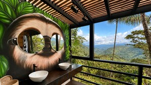 A bathroom with a large mirror, two sinks, and a view of a mountainous landscape. - The Naked Jungle Luxury A-Frame w/ Mountain View (La Pinuela)